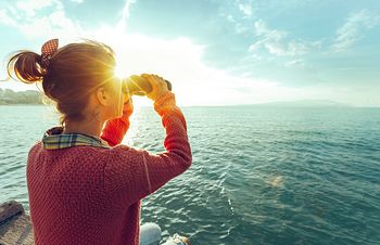 Frau schaut mit Fernglas aufs Meer