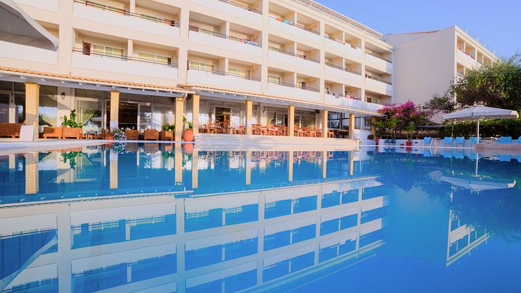 4 stöckiges weißes Hotelgebäude mit Balkonen und einem Pool